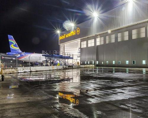 Exterior of Lufthansa Technik Heavy Maintenance Facility at night. Airplane entering hangar in the back.